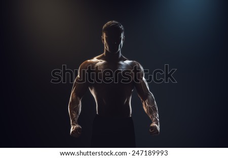 Silhouette of a strong fighter. Confident young fitness man with strong hands and clenched fists. Dramatic light. Royalty-Free Stock Photo #247189993