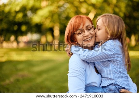 Little girl and her mother enjoying nature on a sunny day, giving kisses to her mom.