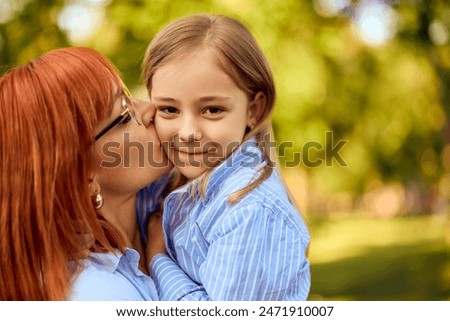 A smiling little girl getting kisses from her mom at the park, spending time together.