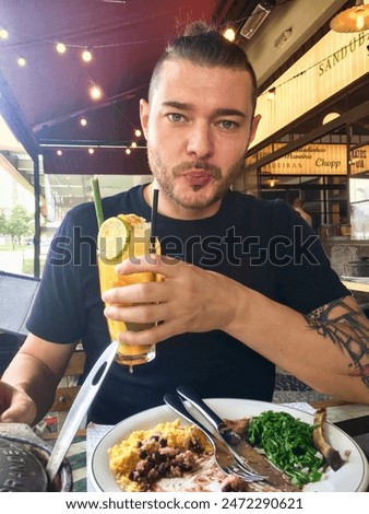 Brazilian man with tattooed arm enjoying a typical traditional Brazilian meal in an outdoor cafe with a passion fruit caipirinha.