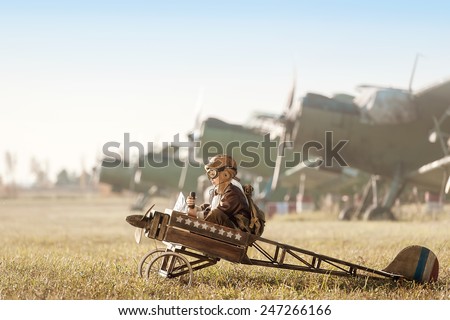 Young Aviator sits in his makeshift toy airplane on airport parking Royalty-Free Stock Photo #247266166