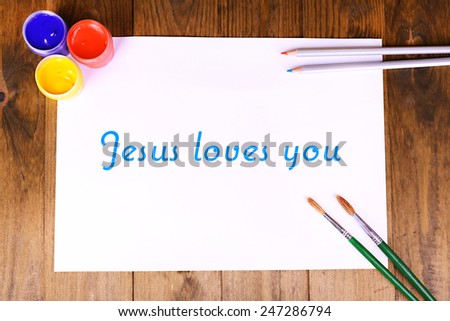 Jesus loves you text on paper on wooden table background