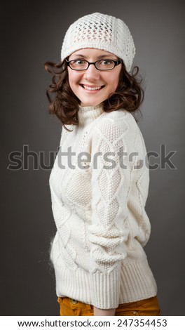 Portrait of a charming young smiling brunette wearing chochet hat and spectacles on studio grey background