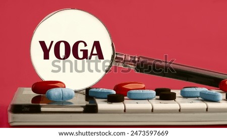 The word YOGA written through a magnifying glass on a calculator with pills on it on a red background with a white spot from a magnifying glass