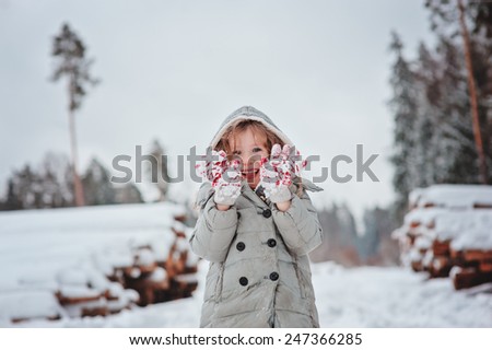 winter portrait of happy child girl shows her gloves in snowy forest with tree felling on background