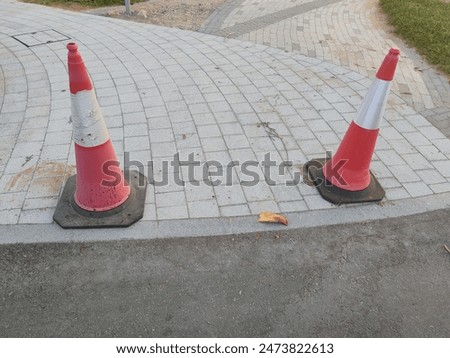 Safety Cones or traffic cone, with white and orange stripes on gray asphalt and Interlocks. 
Red safety cones used for Warning and caution. Two orange safety cones. 