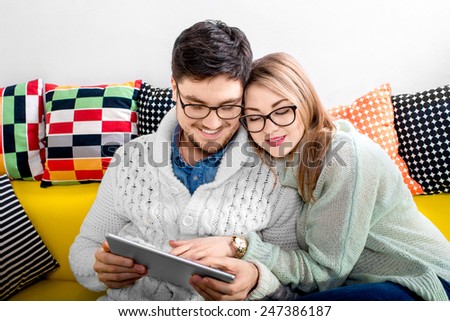 Young couple in sweater and eueglasses with tablet sitting on the couch at home