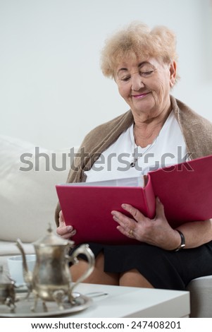 Elderly woman holding album and watching pictures