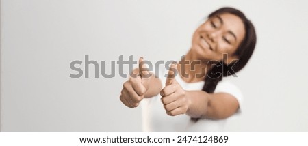 African American girl is shown in the photograph with her arm raised, giving a thumbs up gesture on a plain white background. She is smiling and appears to be expressing approval or agreement.