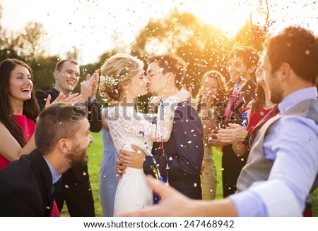 Full length portrait of newlywed couple and their friends at the wedding party showered with confetti in green sunny park Royalty-Free Stock Photo #247468942