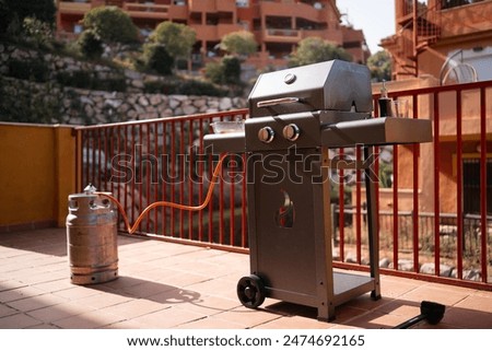 A gas grill connected to a propane tank on a sunny terrace, ready for a barbecue