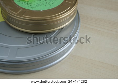 Dusty from storage, a pair of 35mm celluloid film cans on wooden table, one larger silver can and a smaller gold can, complete with a green paper label