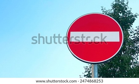 I see a red road sign with a white line. Its for motor vehicles, has a circular background and a font. Its by the road with trees and a sky behind