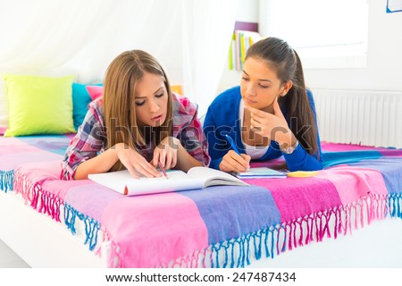 Two female students lying on bed and learning