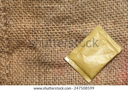 Sugar pack put on the coffee bean sack or gunny sack  brown color represent texture surface background.