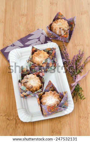 cupcakes in paper origami wrapper on a white plate with a bouquet of flowers next to heather