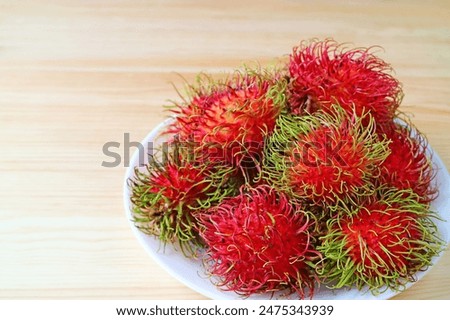 Plate Full of Bright Red Color Ripe Rambutan Fruits Isolated on Wooden Table