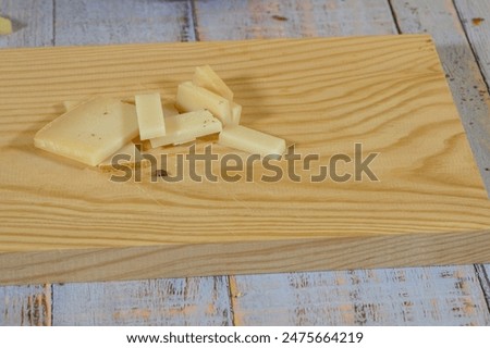 Small pieces of semi-cured cheese and two larger slices on a light wooden cutting board on a table of faded rustic wooden planks.