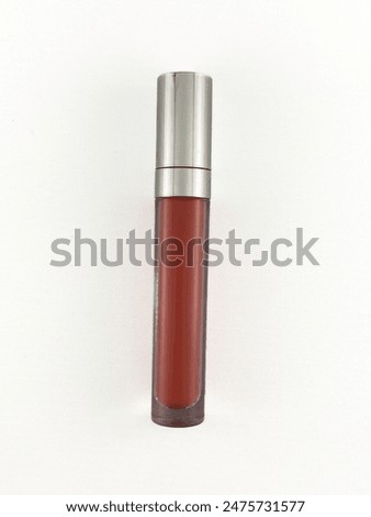 A photo of a brown liquid lipstick with a silver cap. The lipstick is on a white background. The photo is taken from a high angle. The lipstick is in focus and the background is blurred.