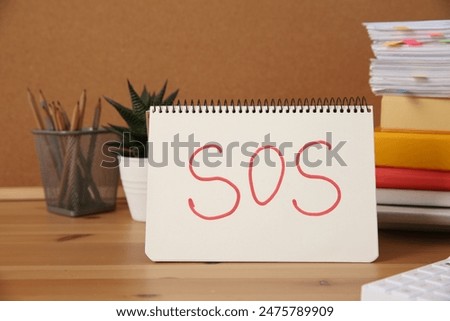 Notebook with word SOS and stationery on wooden table at workplace