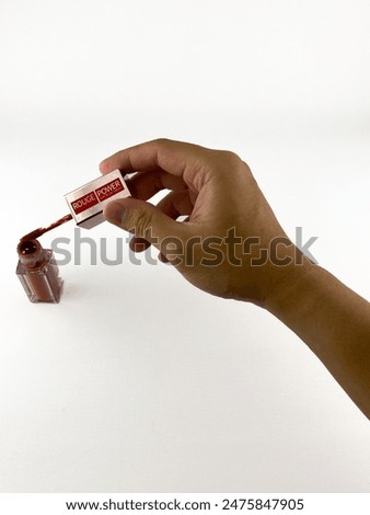 a hand holding a tube of lip gloss. The tube is red and has a clear cap. hand holding the tube by the cap and is unscrewing it. tube is labeled Rouge Power and has a picture of a woman's lips on it