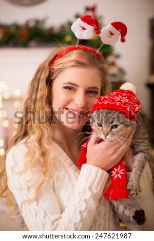 Young girl near a new-year tree with a cat in the cap of Santa