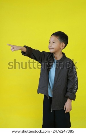 Portrait of Asian little boy wear a jacket and pointing beside isolated on yellow studio background.