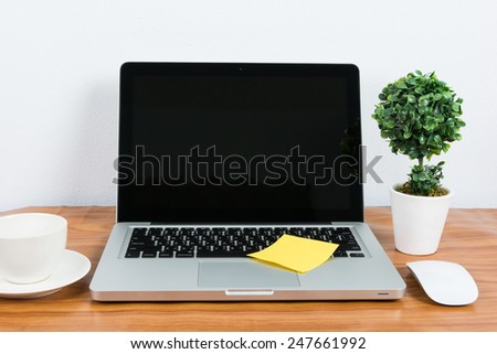 Laptop and flower pot on wooden table on wall background