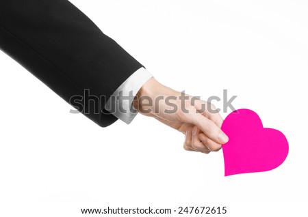 Valentine's Day and love theme: a man in a black suit holding a pink heart isolated on a white background in studio