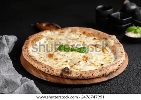 Cheese and basil pizza on wooden board surrounded by black dishes