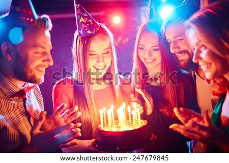 Pretty girl with birthday cake and her friends looking at burning candles at party