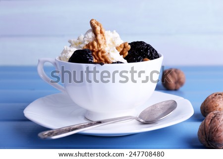 Dessert with prunes and nuts in cup on color wooden table background