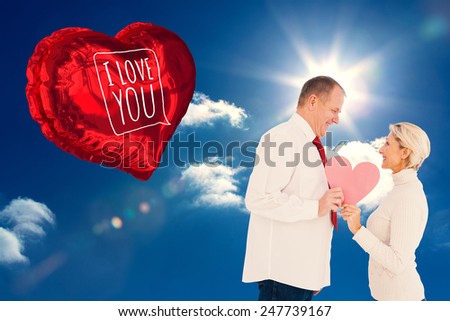 Older affectionate couple holding pink heart shape against sky