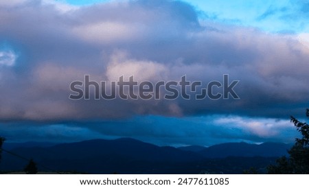 The serene beauty of dusk, a tranquil mountain range under a spectacular sky. The interplay of soft evening light and rolling clouds creates a calm yet dynamic scene, perfect for any project