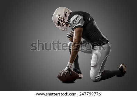 Football Player with a black uniform on his knees, on a black background.
