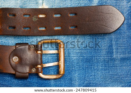 Old leather belt with a buckle on the jeans background with copy space