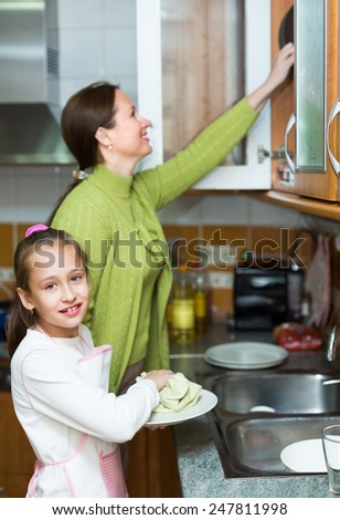 Smiling preschooler daughter helping mother washing dishes in the kitchen 