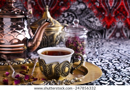 Tea in a beautiful metal Cup with Oriental motifs on the metal tray surrounded by dried rose buds