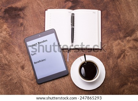 A Tablet with the inscription "Payment transfers", notepad with pencil and coffee on a table