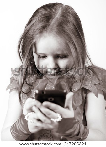 Cute little girl dressed in ball gown playing with smartphone and smiling, isolated on white background