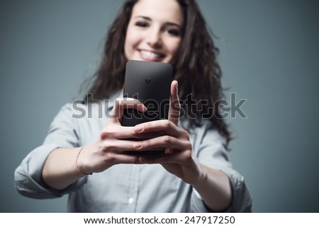 Young smiling woman taking pictures with a mobile touch screen phone