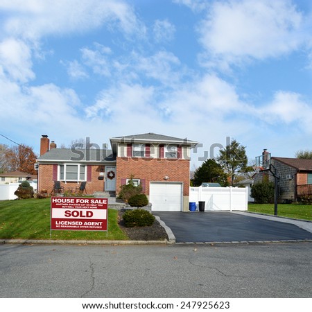 Real estate sold (another success let us help you buy sell your next home) sign Beautiful Suburban Brick Snout style home landscaped yard residential neighborhood USA blue sky clouds