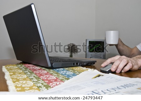 Low angle shot of laptop with man (out of the shot) holding mouse and coffee cup, watching stock graphic on TV.