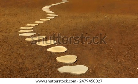 A winding path of white stepping stones on reddish-brown sandy ground.