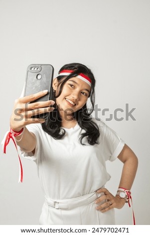A beautiful young woman in a white t-shirt is holding her cell phone with her left hand on her waist. Indonesian woman selfie concept