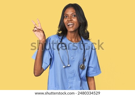 Young Indian nurse with stethoscope joyful and carefree showing a peace symbol with fingers.