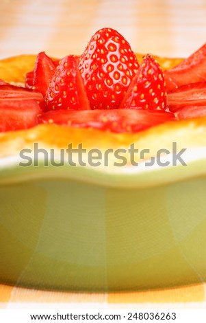 Extreme closeup of a strawberry and custard tart in a green baking dish over a white and yellow checkered background.