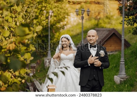 A bride and groom are walking down a path in a garden. The bride is wearing a white dress and the groom is wearing a black suit. Scene is happy and romantic, as the couple is getting married