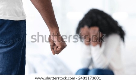 A mans fist is raised in a threatening manner towards a woman who is crying and covering her face.