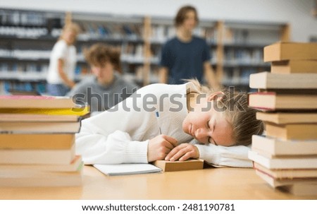 Tired girl fell asleep at table with textbooks in the school library